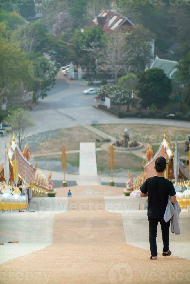 costas do jovem homem caminhando baixa escadas ao longo corredor para alcance dele desejado destino depois de caminhando acima escadas para pagar homenagem para Buda imagem de acordo com para crença e poder do budismo. foto