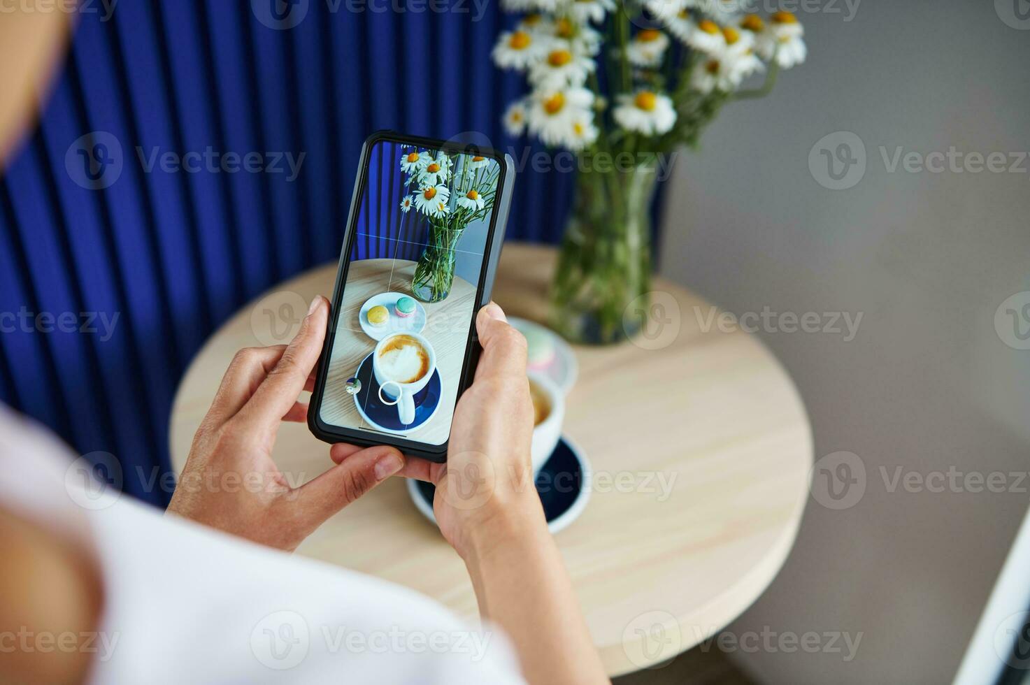 mulher levando uma Comida fotografia do servido mesa com macarons e copo do café café com leite ou cappuccino dentro à moda café casa. Móvel telefone dentro viver Visão modo foto