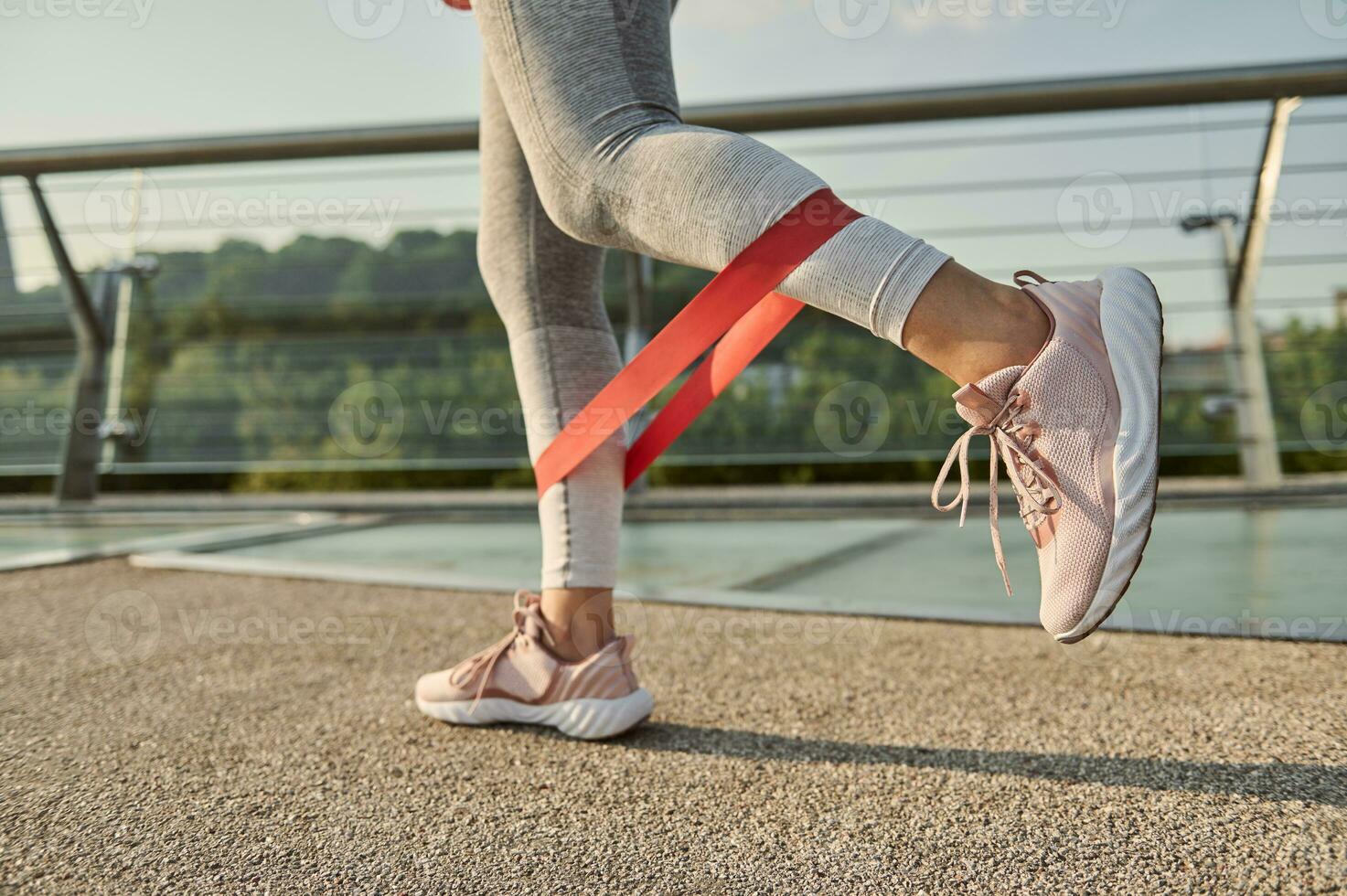 fechar-se do a pernas do a atleta fazendo corpo peso Treinamento com uma resistência ginástica elástico banda em uma cidade ponte. foto