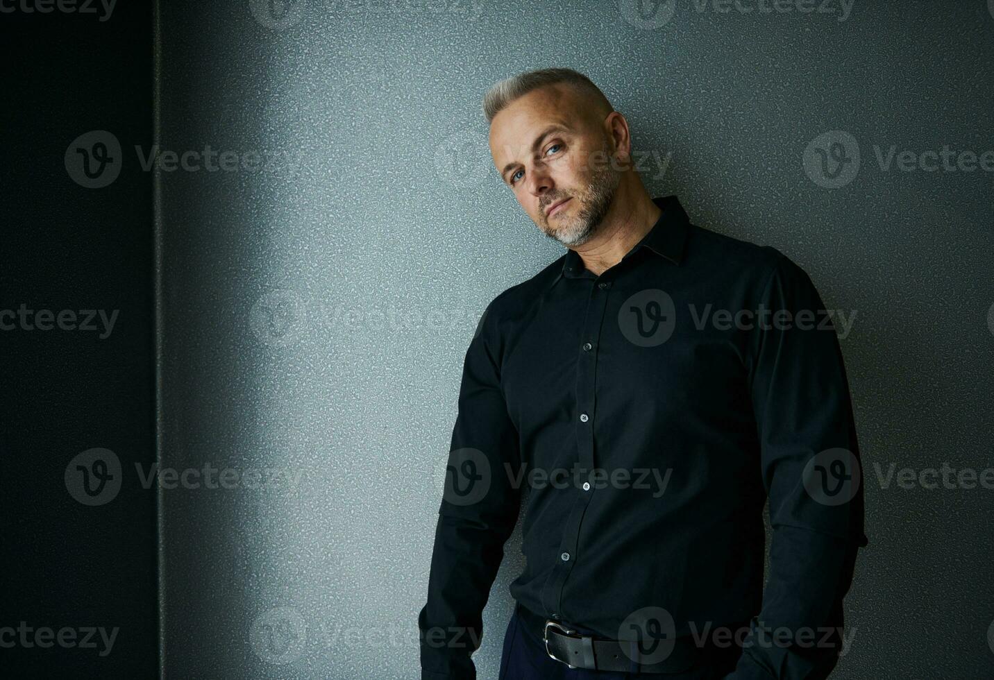 atraente bonito meio envelhecido caucasiano homem dentro Preto casual terno posando contra cinzento fundo, com confiança olhando às Câmera. cópia de espaço foto