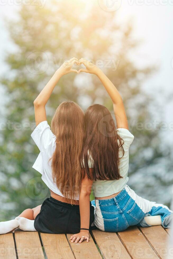 costas Visão do jovem meninas sentar em uma terraço às uma altura dentro a montanhas contra a pano de fundo do névoa e montanhas foto