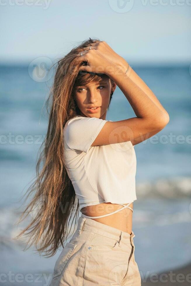 adorável jovem menina com lindo grandes cabelo apreciar tropical de praia período de férias. a menina em a Beira Mar às pôr do sol foto