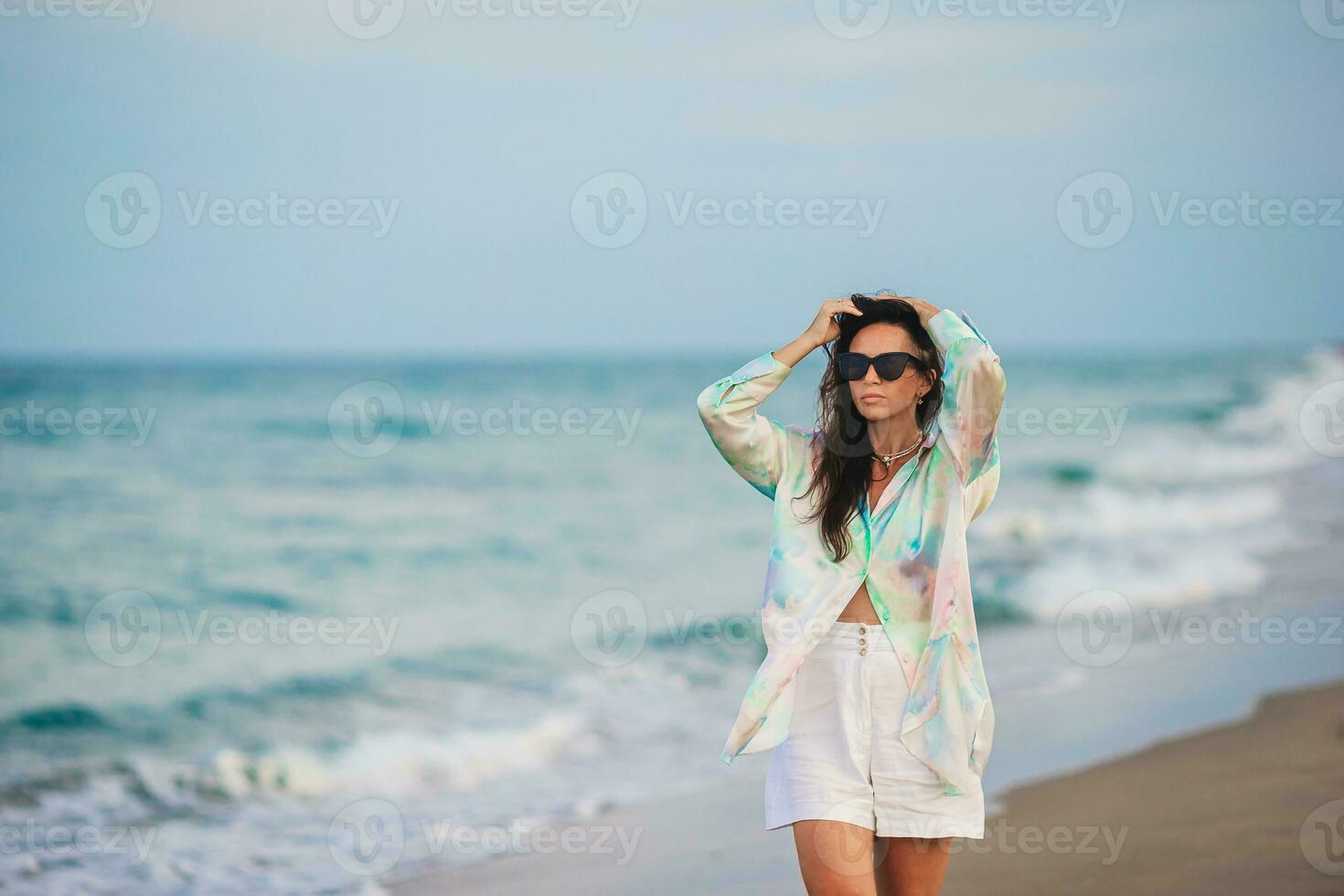 jovem feliz mulher em a de praia apreciar dela verão período de férias. mulher caminhando ao longo a mar dentro tarde. foto