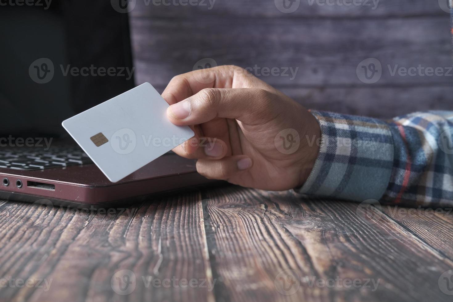 homem com as mãos segurando um cartão de crédito e usando laptop para fazer compras online foto