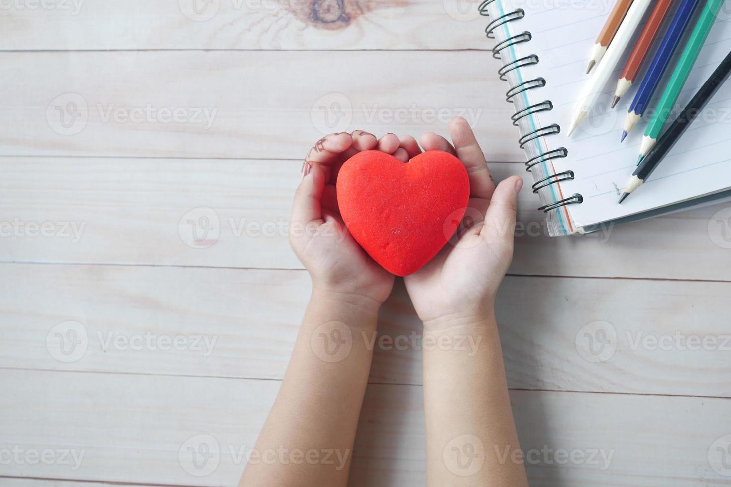 criança segurando coração vermelho na mesa foto