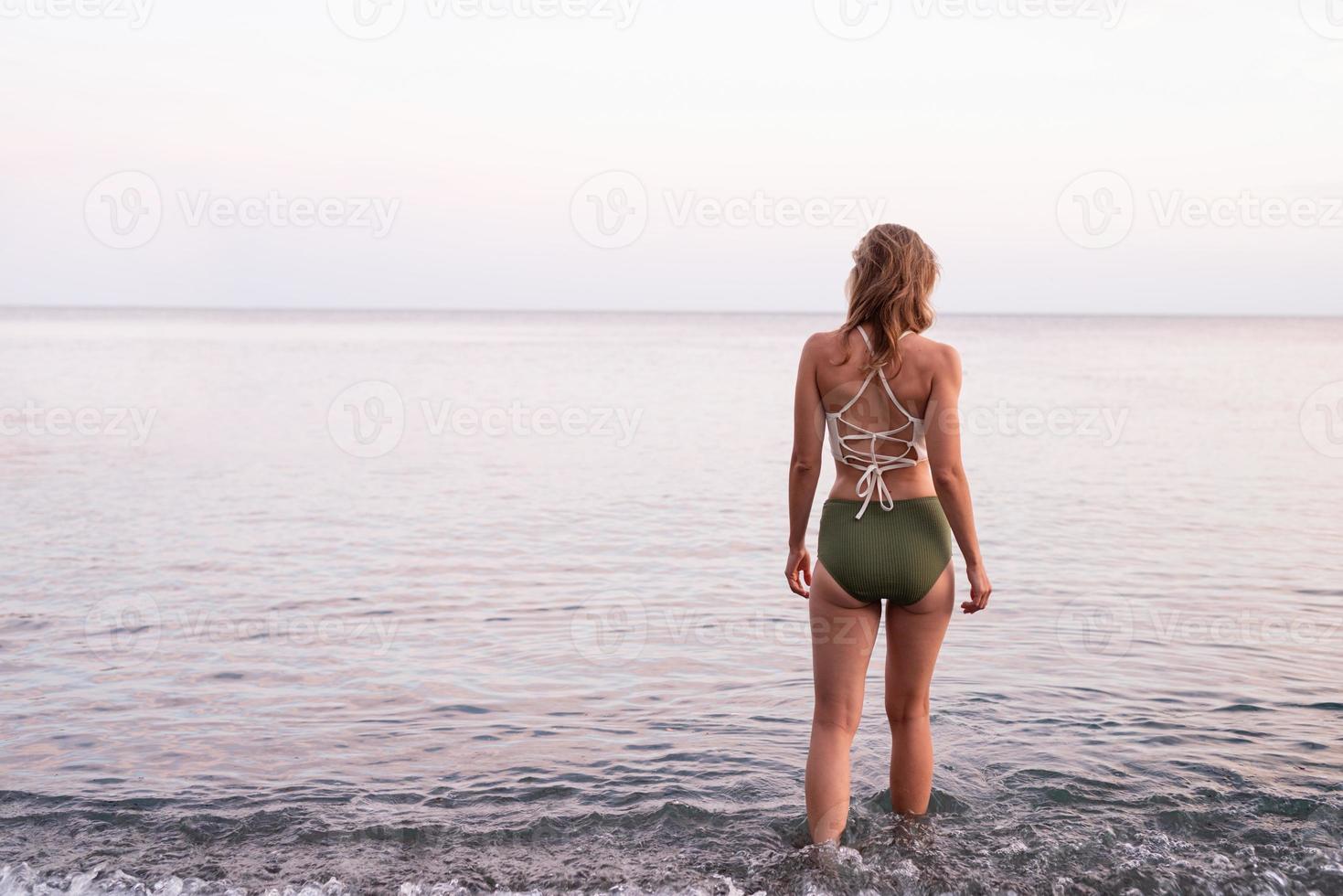 vista traseira de uma jovem em pé na praia pedregosa, olhando para o mar foto