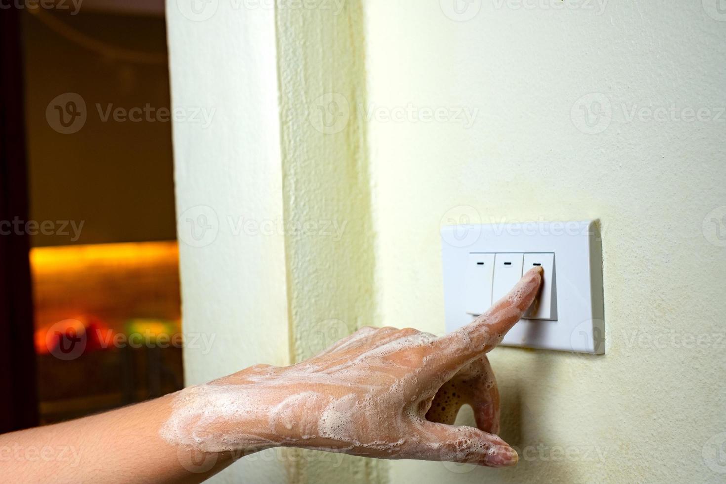 mão molhada acende as luzes e o interruptor elétrico no fundo da parede branca foto