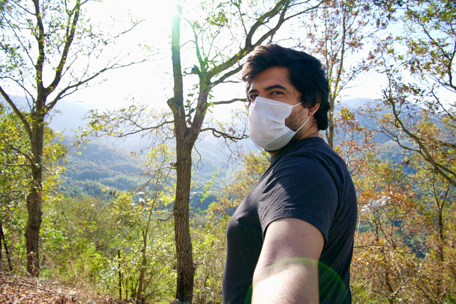 homem usando uma máscara facial e tira uma selfie na natureza. foto