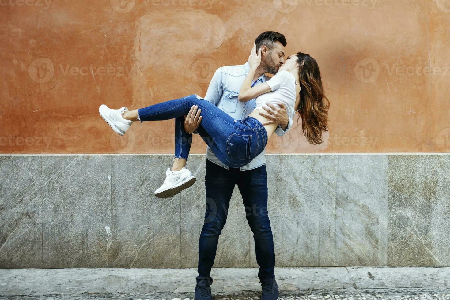despreocupado casal dentro amor se beijando dentro frente do uma parede ao ar livre foto