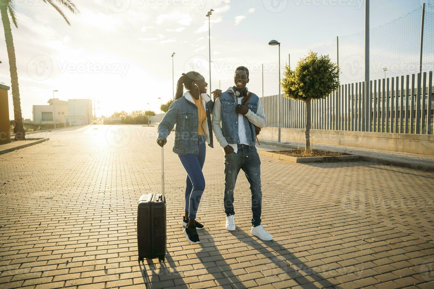 feliz heterossexual casal com rodado bagagem caminhando em rua durante ensolarado dia foto