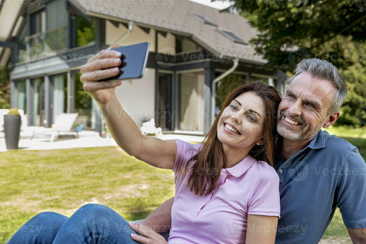 feliz casal sentado dentro jardim do seus casa levando uma selfie foto