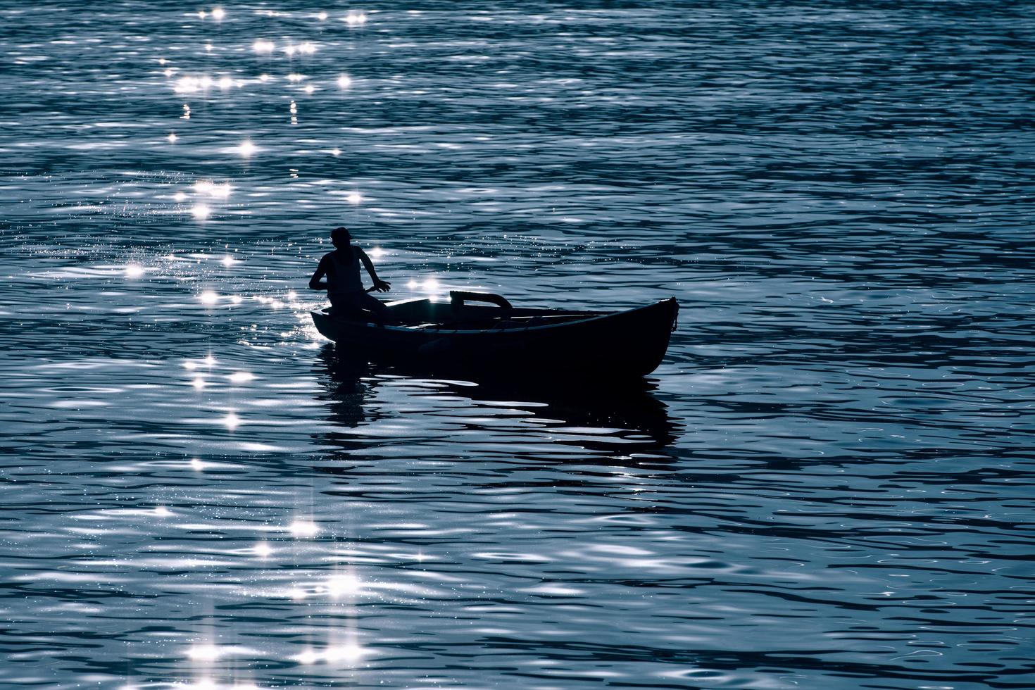 pequeno barco no lago em silhueta com reflexos dos raios solares foto