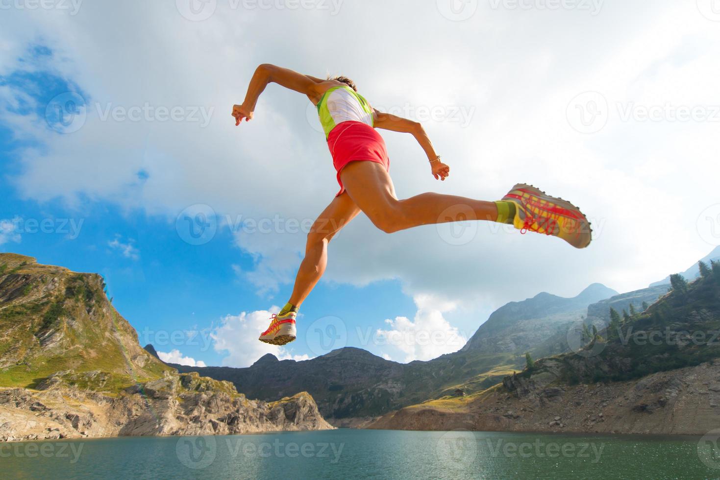 pulando garota enquanto ele corre perto de um lago na montanha foto