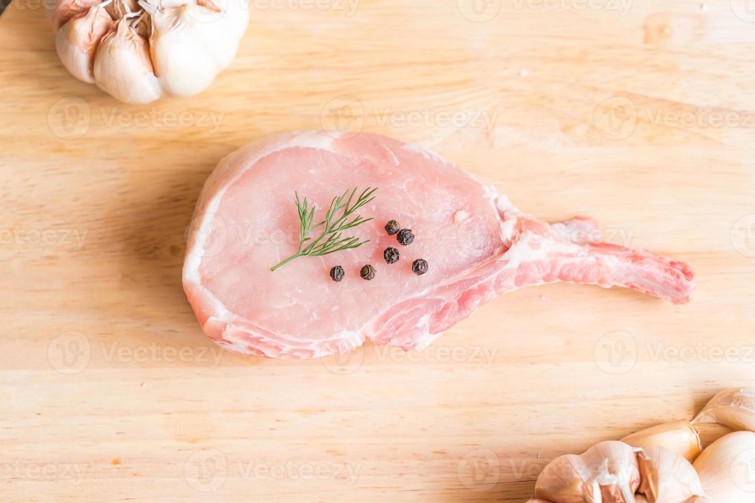 Costeleta de porco fresca na tábua de madeira com alho e pimenta preta foto