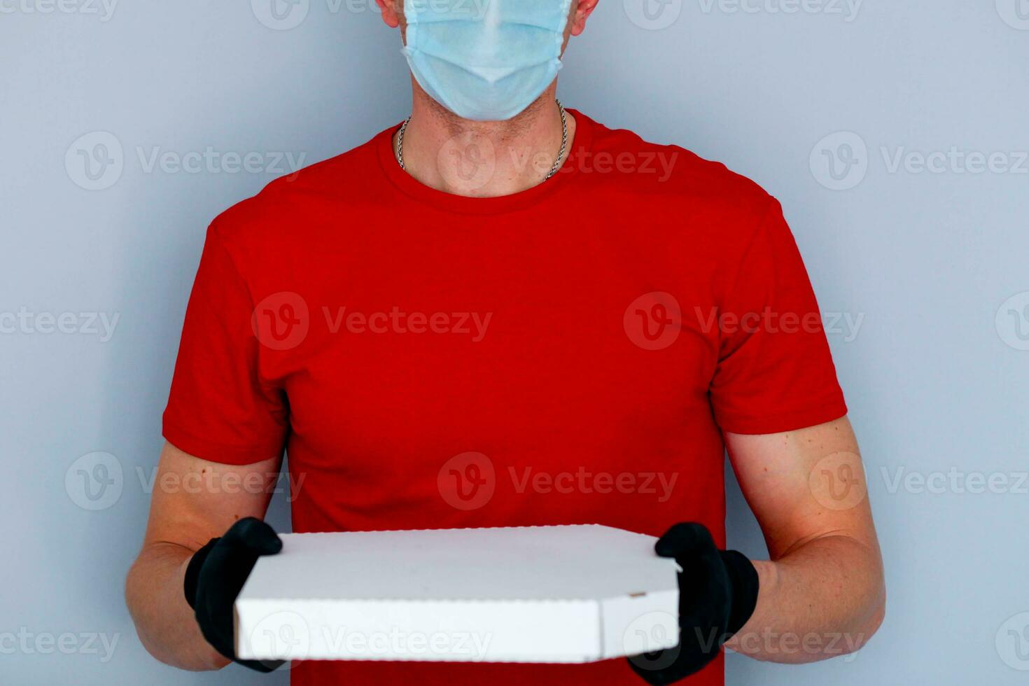 Entrega homem empregado dentro vermelho boné em branco camiseta uniforme face mascarar luvas aguarde cartão caixa pizza em cinzento fundo serviço quarentena pandemia coronavírus vírus 2019-ncov conceito. foto