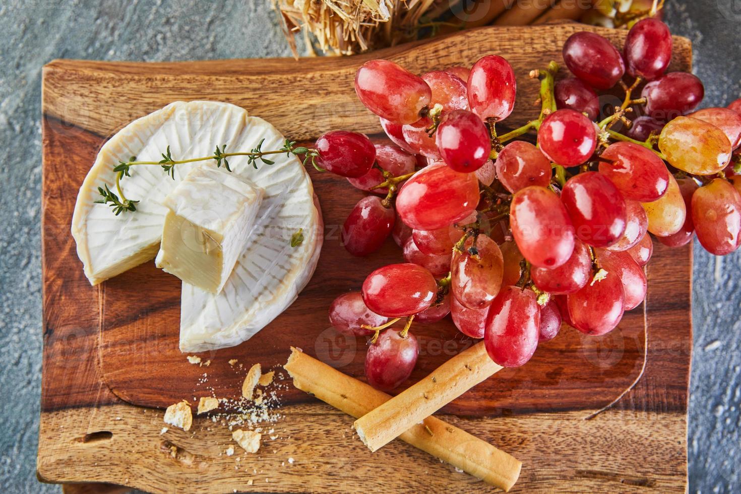 queijo brie com alho e uvas em suporte de madeira foto