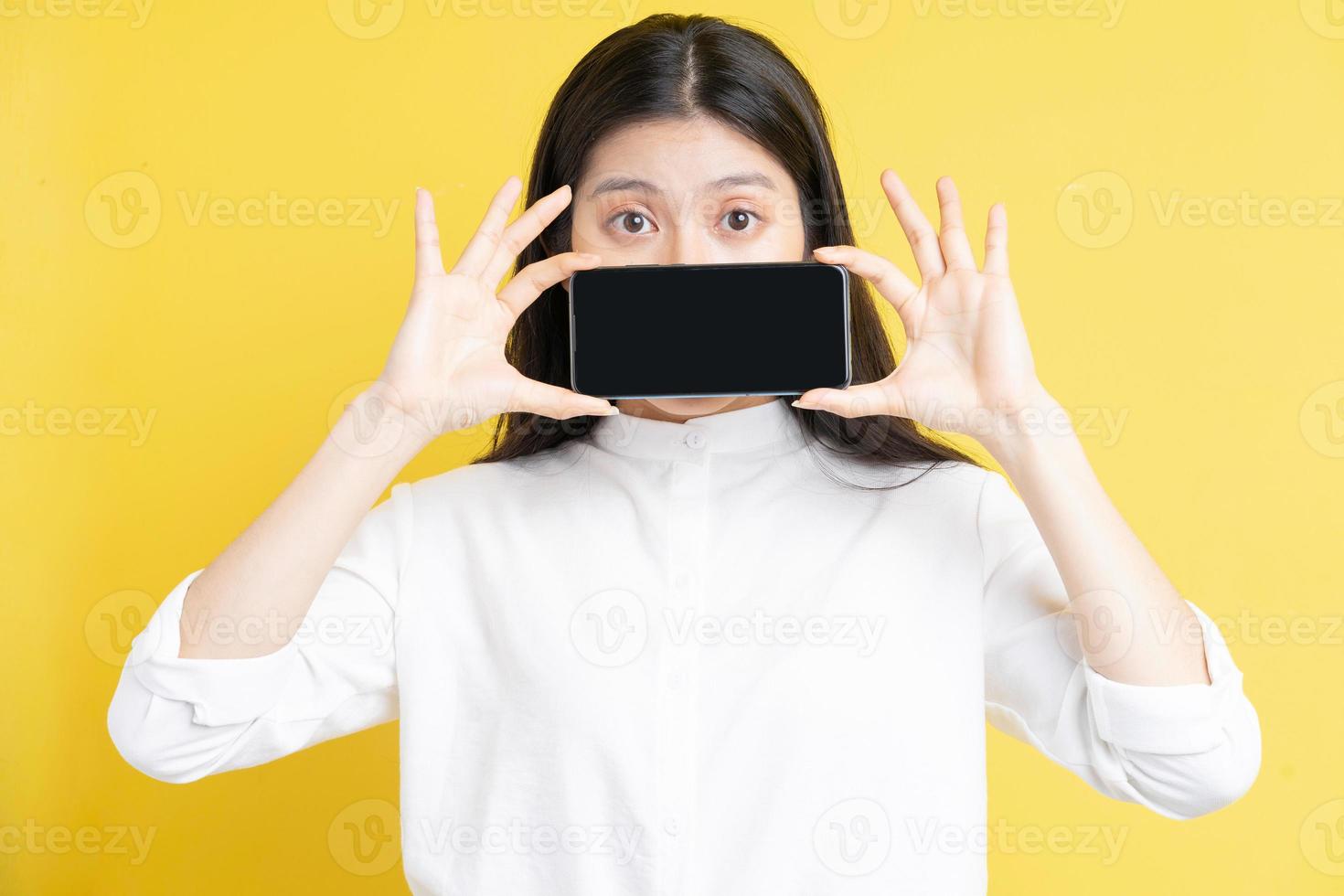 jovem asiática segurando um telefone com expressão em fundo amarelo foto