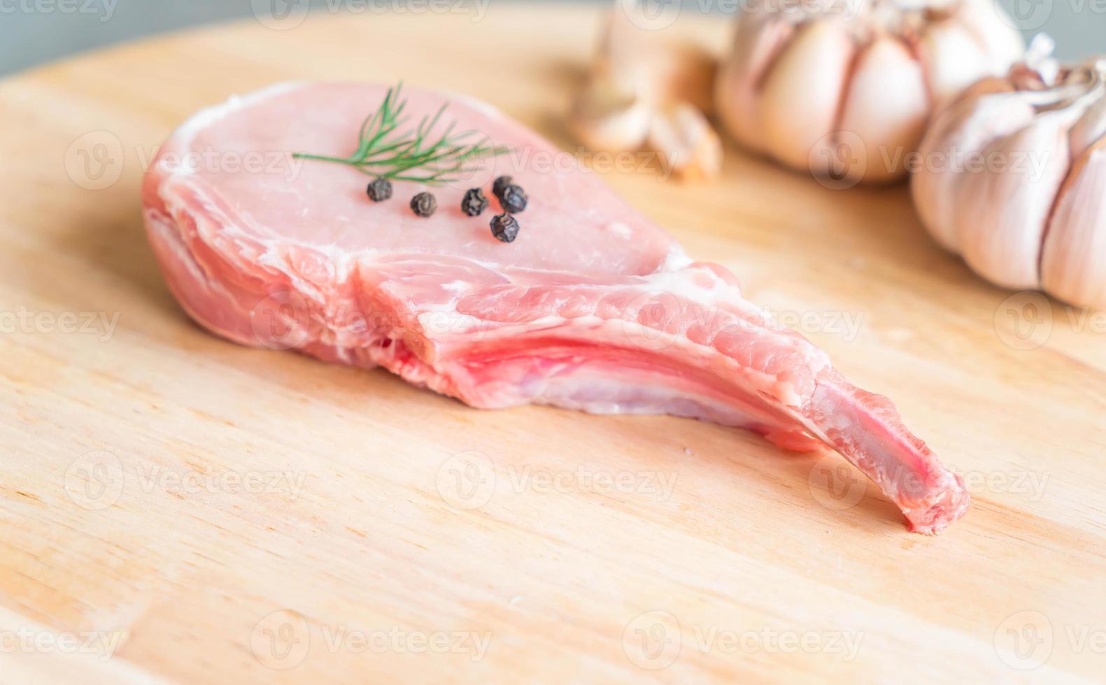 Costeleta de porco fresca na tábua de madeira com alho e pimenta preta foto