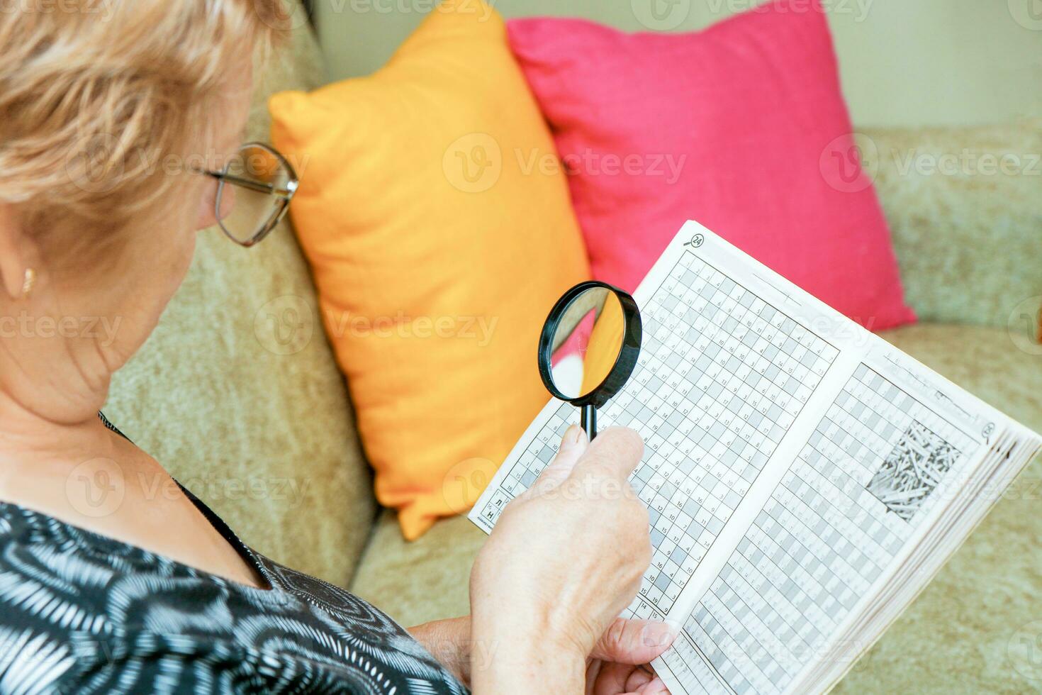 Senior mulher resolve palavras cruzadas quebra-cabeças com uma ampliação vidro foto