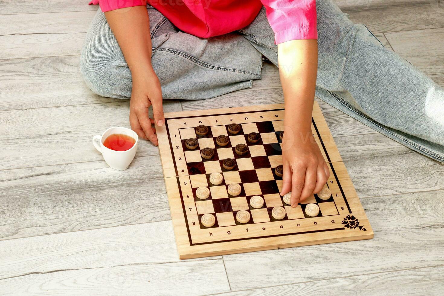 mulher sentado em a chão jogando jogo de damas com ela mesma, Próximo para uma copo do chá foto