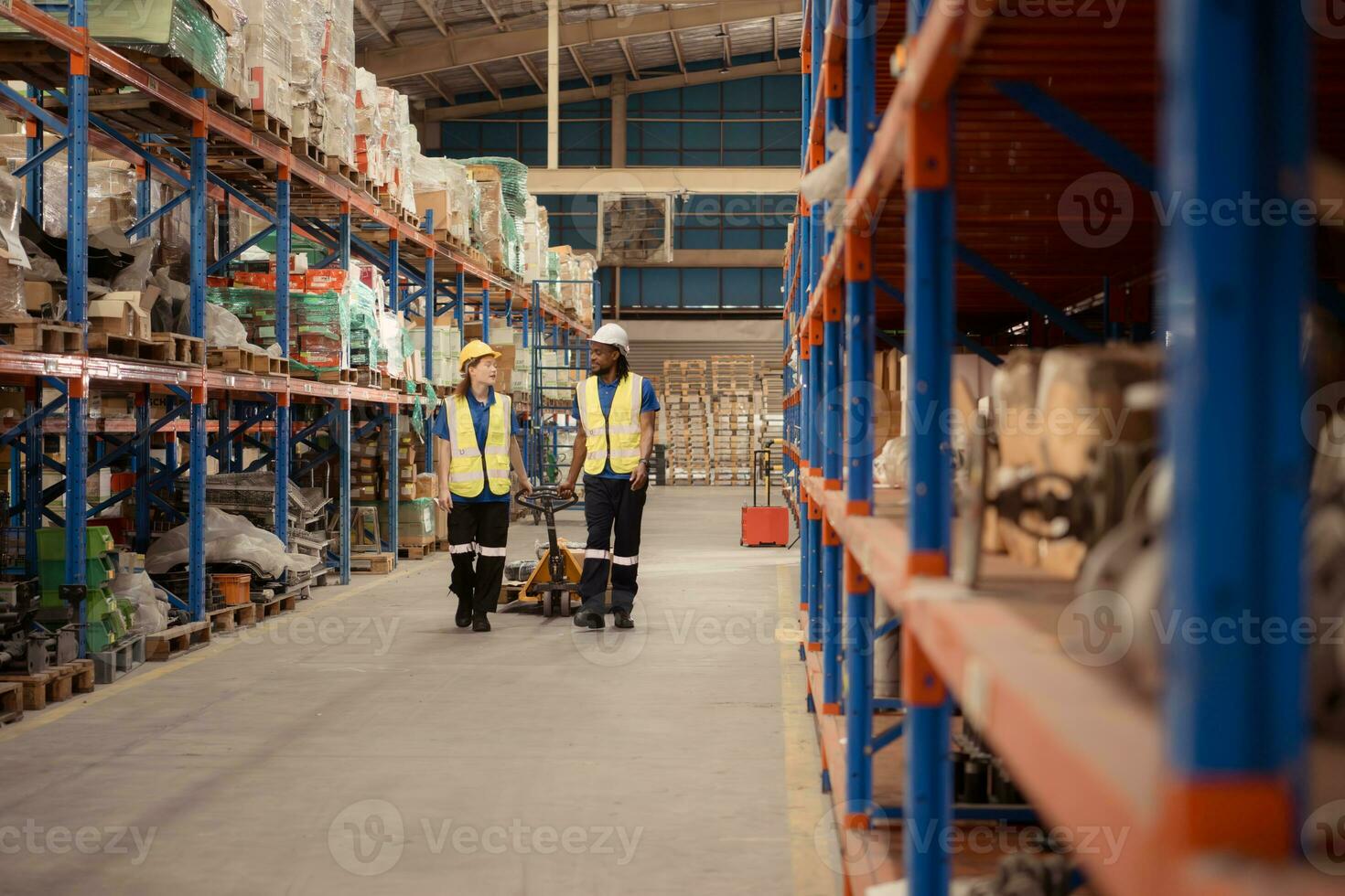 topo Visão do dois armazém trabalhadores empurrando uma palete caminhão dentro uma Remessa e distribuição armazém. foto