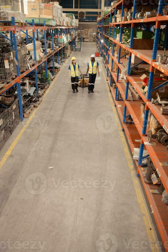 topo Visão do dois armazém trabalhadores empurrando uma palete caminhão dentro uma Remessa e distribuição armazém. foto