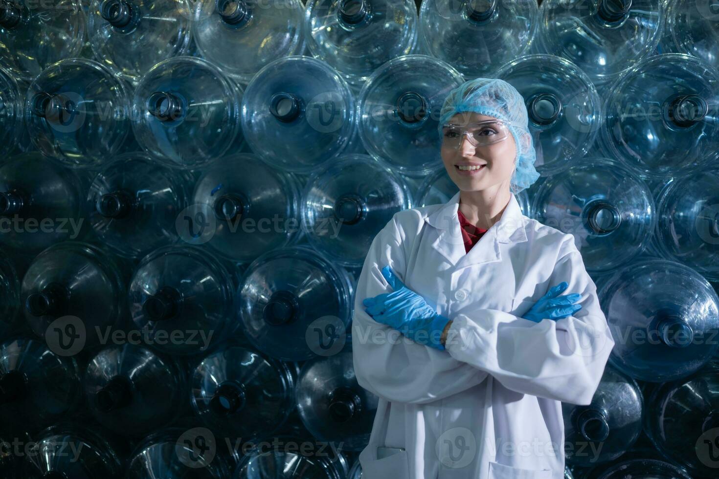 retrato do fêmea cientista com braços cruzado dentro bebendo água fábrica, ela estava em pé dentro frente do uma plástico garrafa. foto