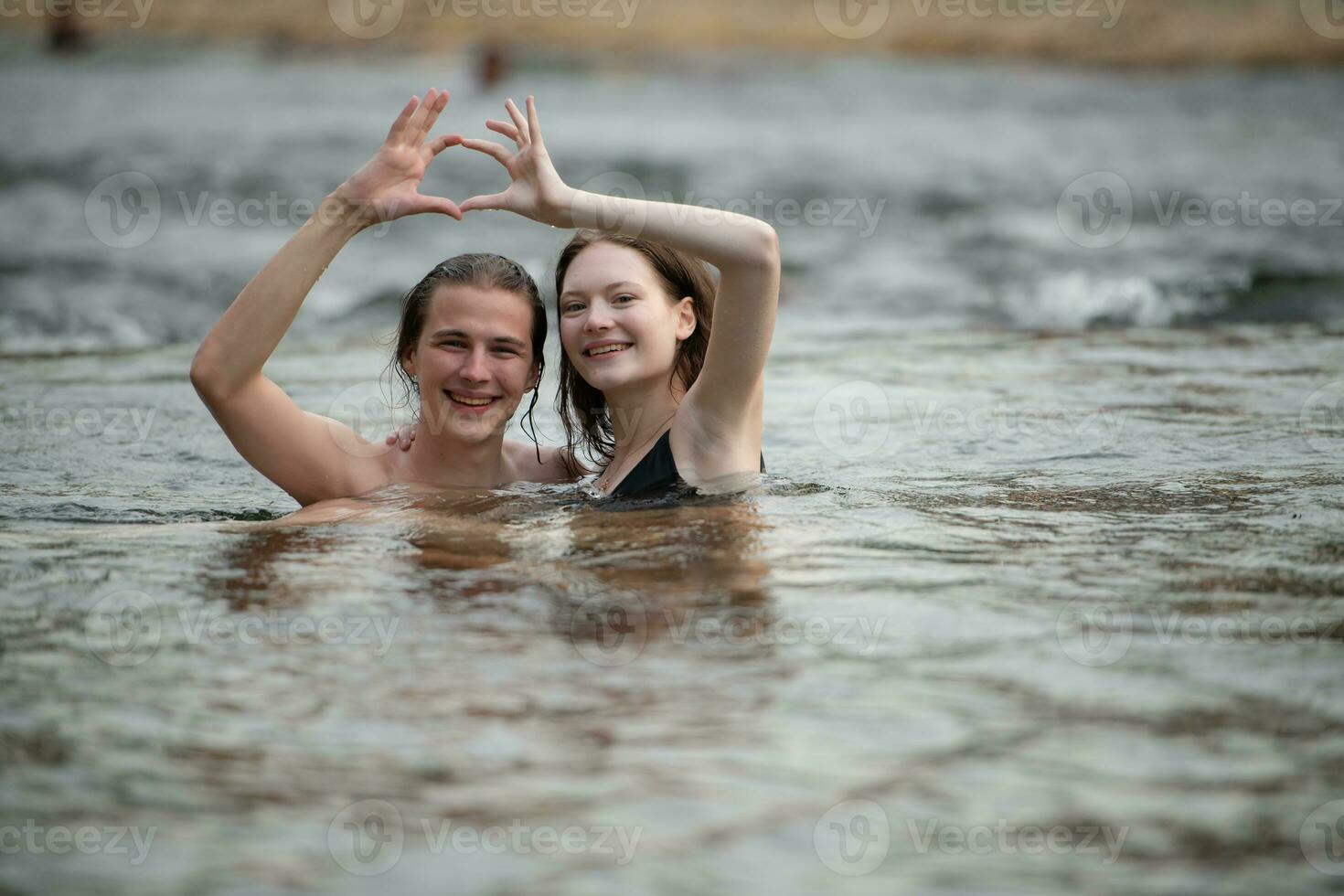 dois jovem meninas dentro a água fazer uma coração com seus mãos. foto