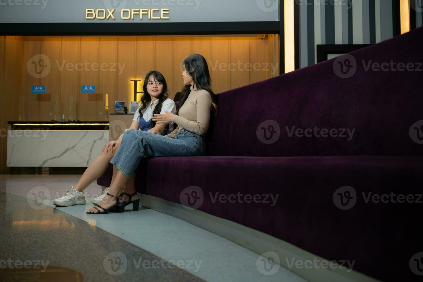 dois jovem ásia mulheres comendo Pipoca e esperando para assistindo filme às frente do caixa escritório foto