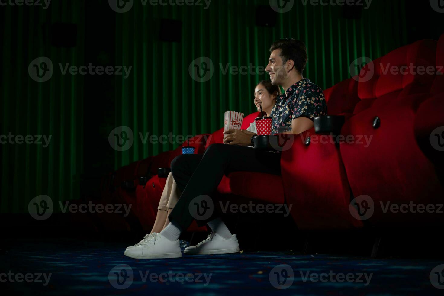 jovem homem e mulher assistindo filme dentro cinema, sentado em vermelho assentos foto