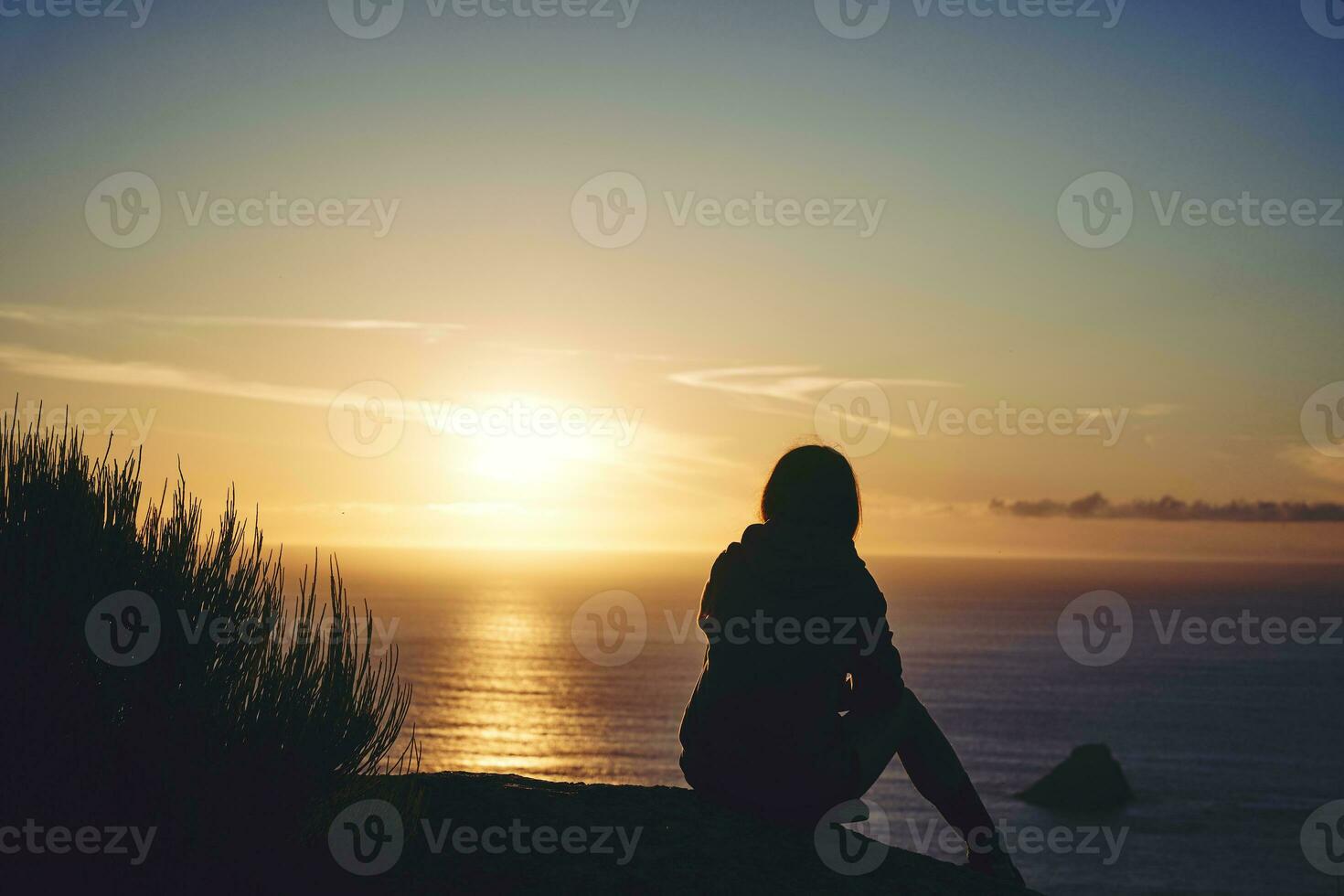 silhueta do uma jovem mulher em uma penhasco assistindo a pôr do sol do a costa do morte foto