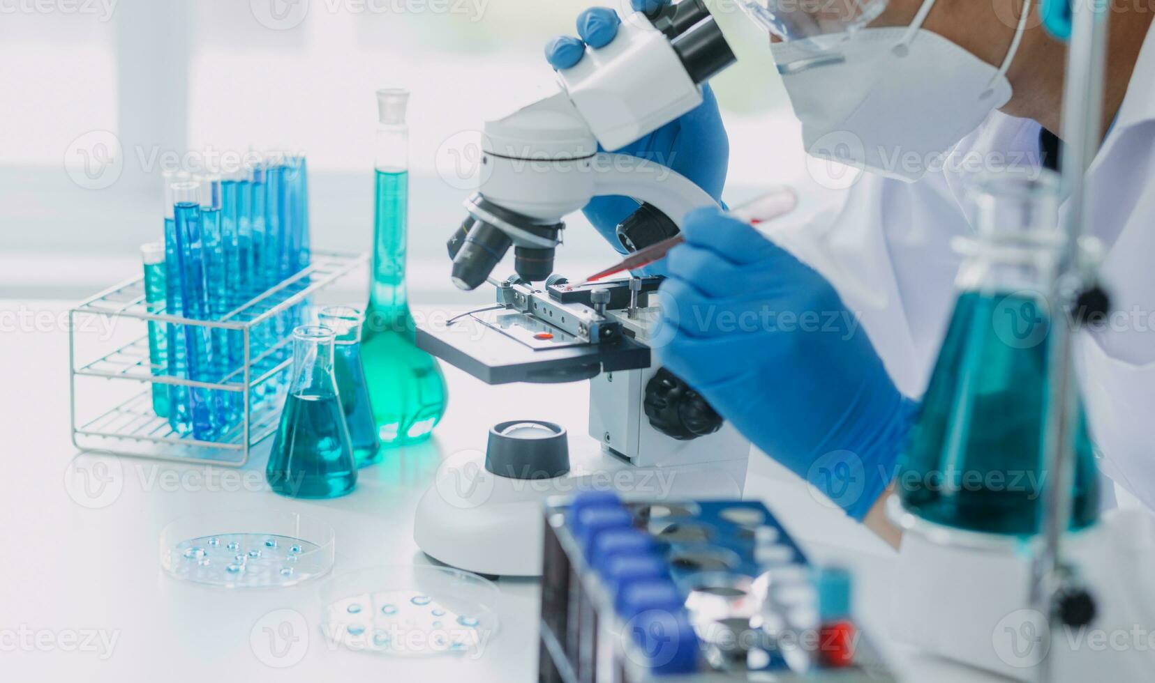 jovem cientistas conduzindo pesquisa investigações dentro uma médico laboratório, uma investigador dentro a primeiro plano é usando uma microscópio foto