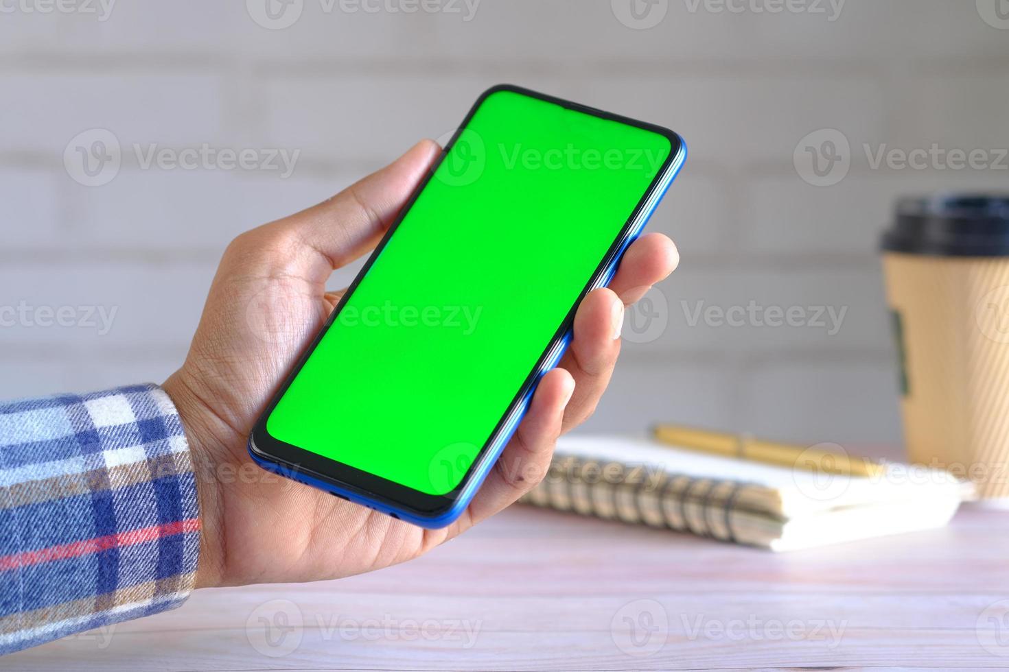 Feche a mão do jovem usando um telefone inteligente com tela verde foto