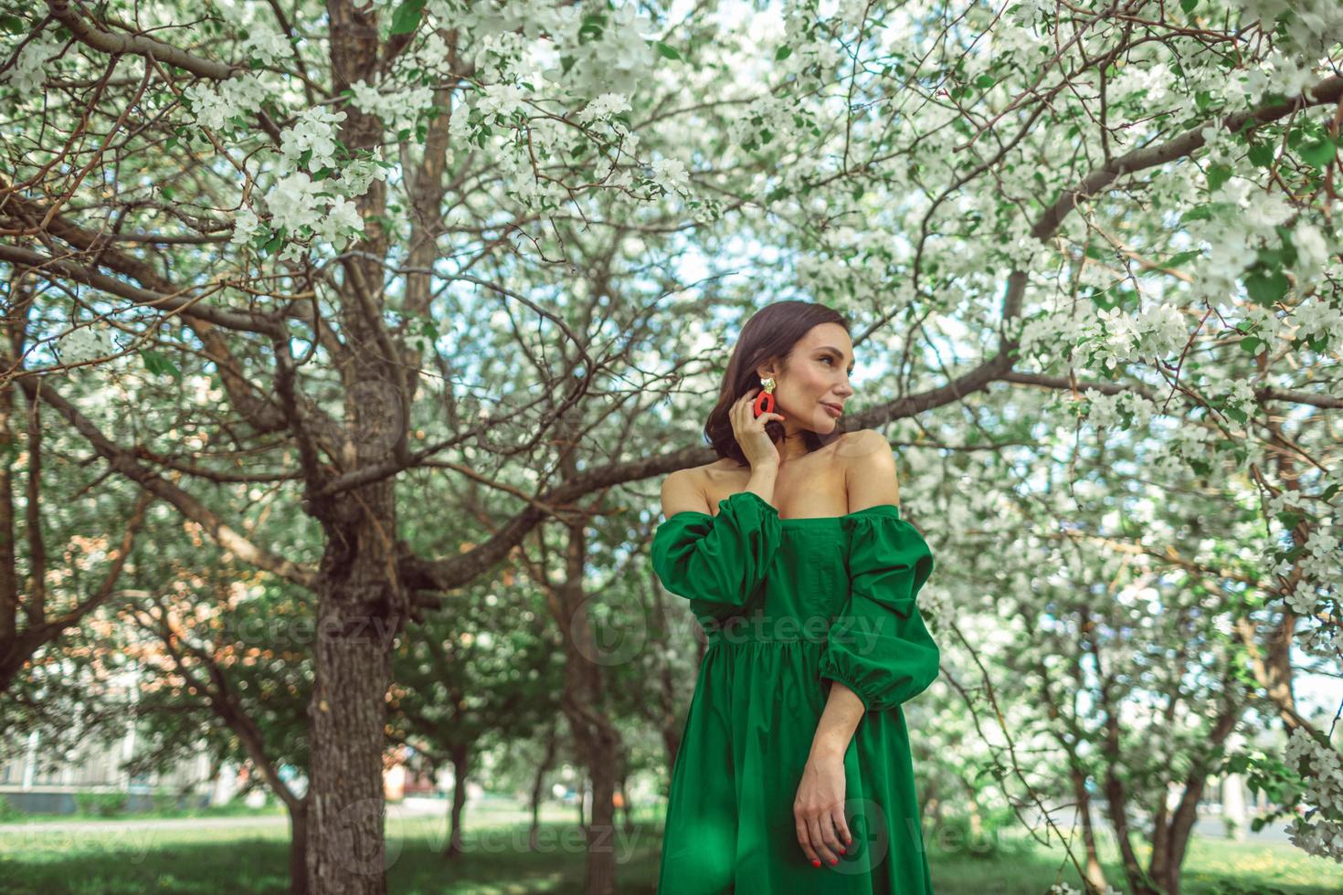 uma jovem está parada no parque sob uma macieira em flor foto