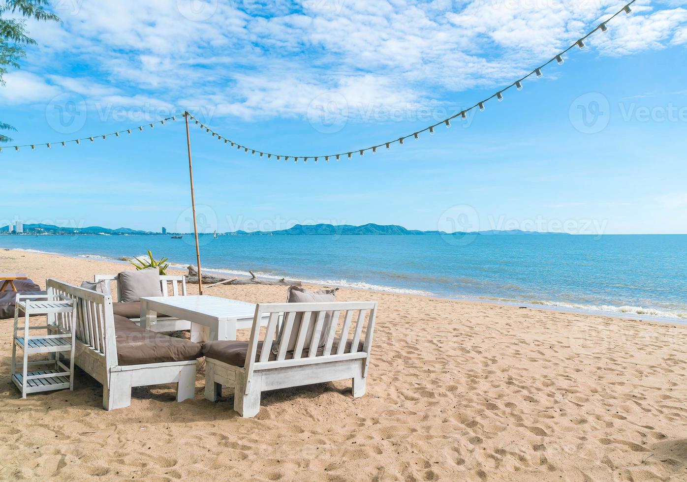 cadeiras e mesa brancas na praia com vista para o mar azul e céu claro foto