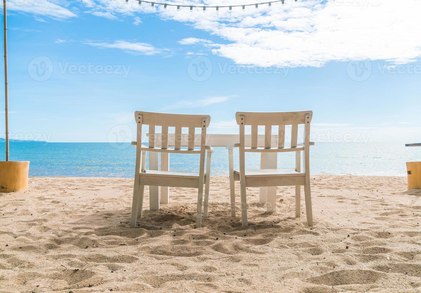 cadeiras e mesa brancas na praia com vista para o mar azul e céu claro foto