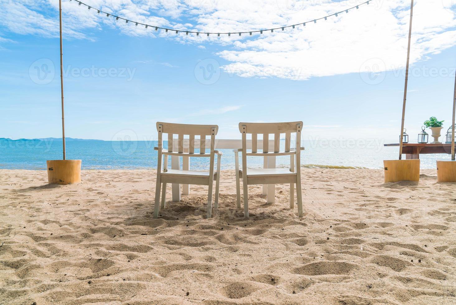 cadeiras e mesa brancas na praia com vista para o mar azul e céu claro foto
