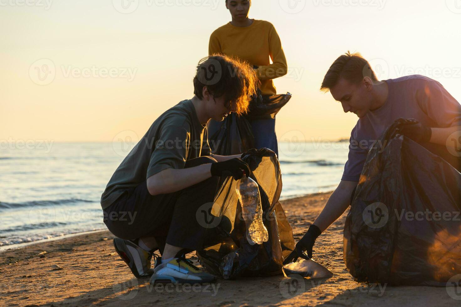 terra dia. voluntários ativistas coleta lixo limpeza do de praia costeiro zona. mulher e mans coloca plástico Lixo dentro lixo saco em oceano costa. de Meio Ambiente conservação costeiro zona limpeza. foto