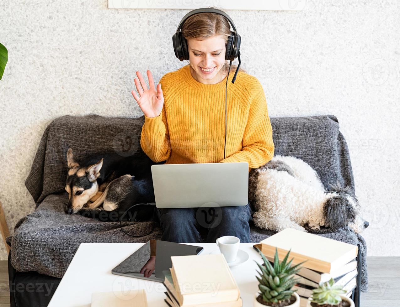 mulher com fones de ouvido pretos estudando on-line usando um laptop e dizendo olá foto