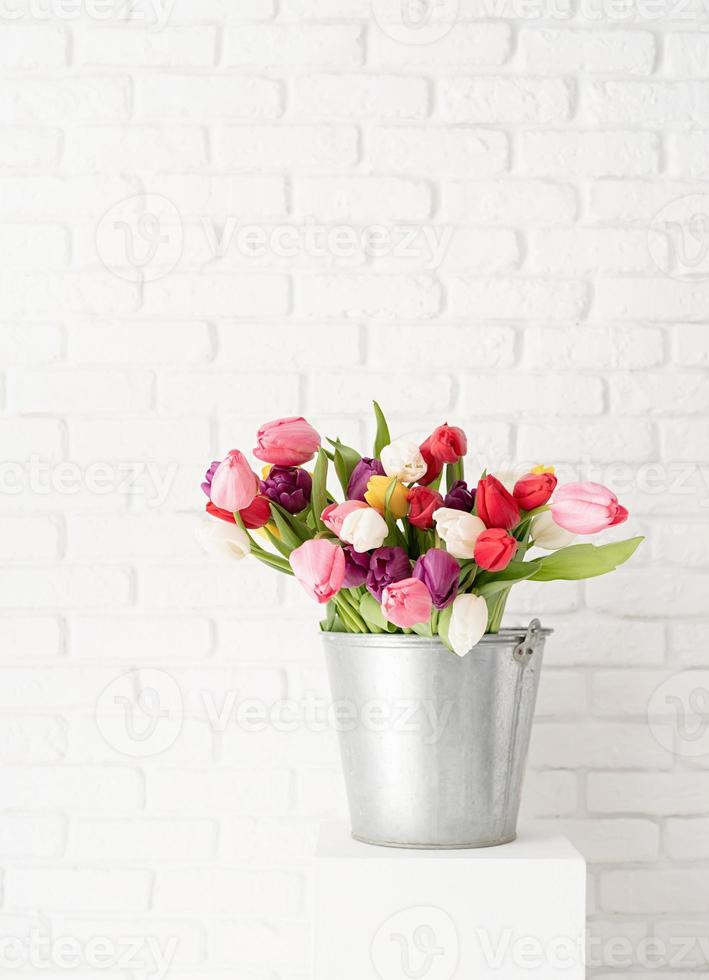 balde de flores de tulipa sobre o fundo da parede de tijolo branco foto