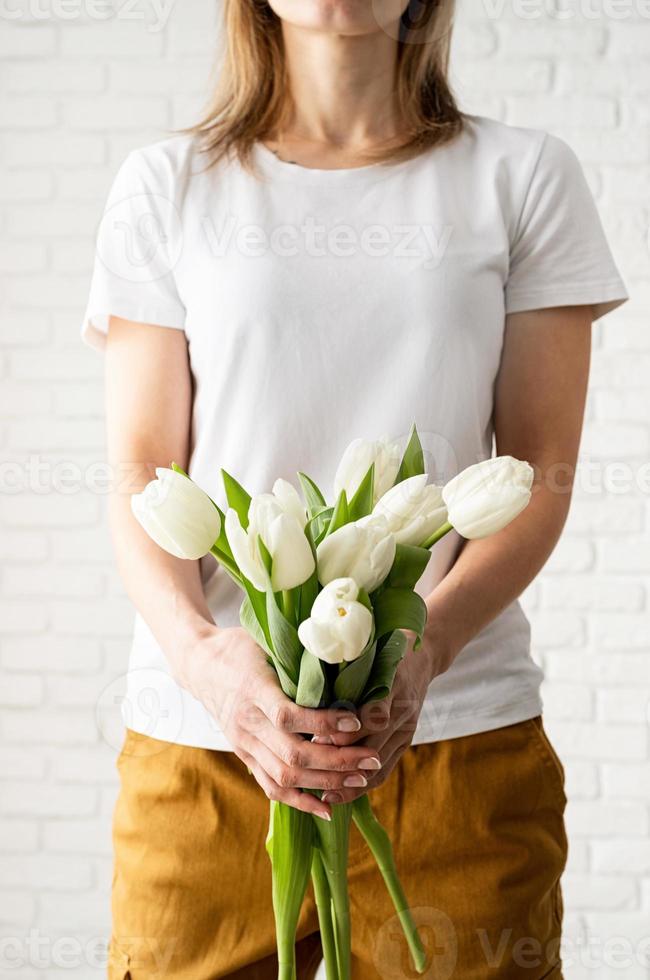 jovem vestindo uma camiseta branca em branco segurando flores de tulipas foto