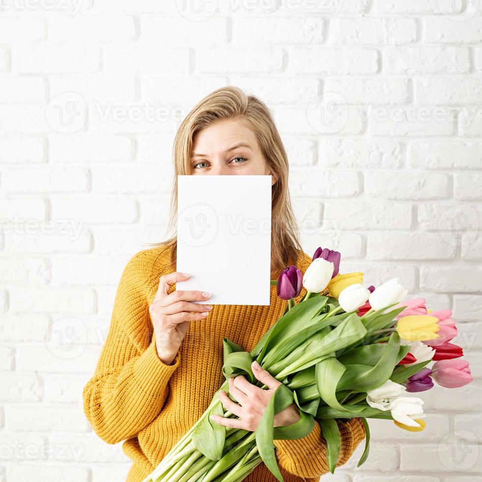 mulher com roupas amarelas segurando um buquê de tulipas e um cartão em branco foto