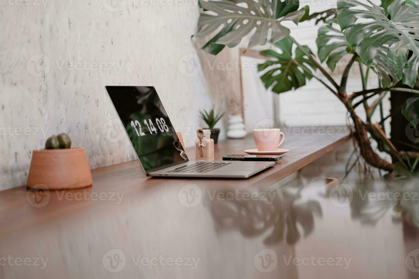 uma computador portátil em a mesa com uma copo do café com monstera folha foto