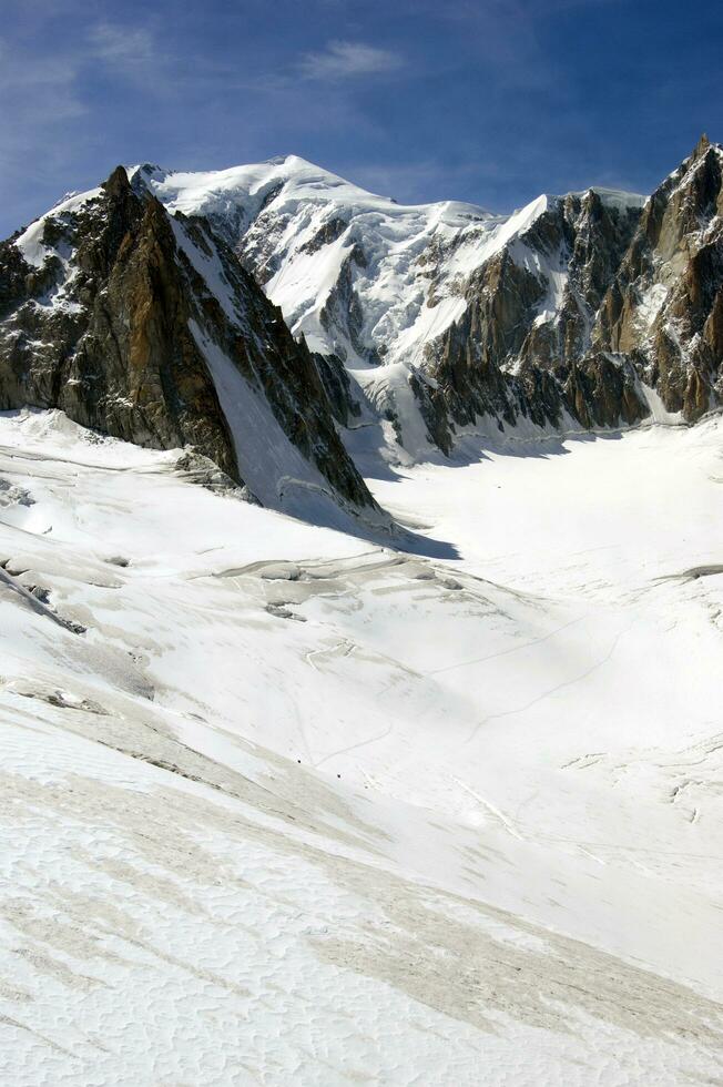 dois pessoas estão caminhada acima uma montanha com neve coberto montanhas foto