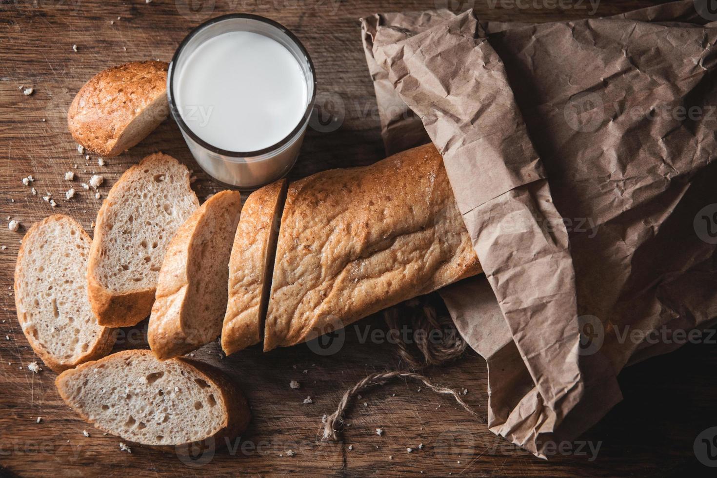 pão com pedaços cortados deitado sobre uma placa de madeira e um copo de leite fresco foto