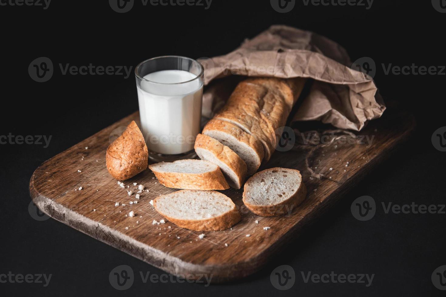 pão com pedaços cortados deitado sobre uma placa de madeira e um copo de leite fresco foto
