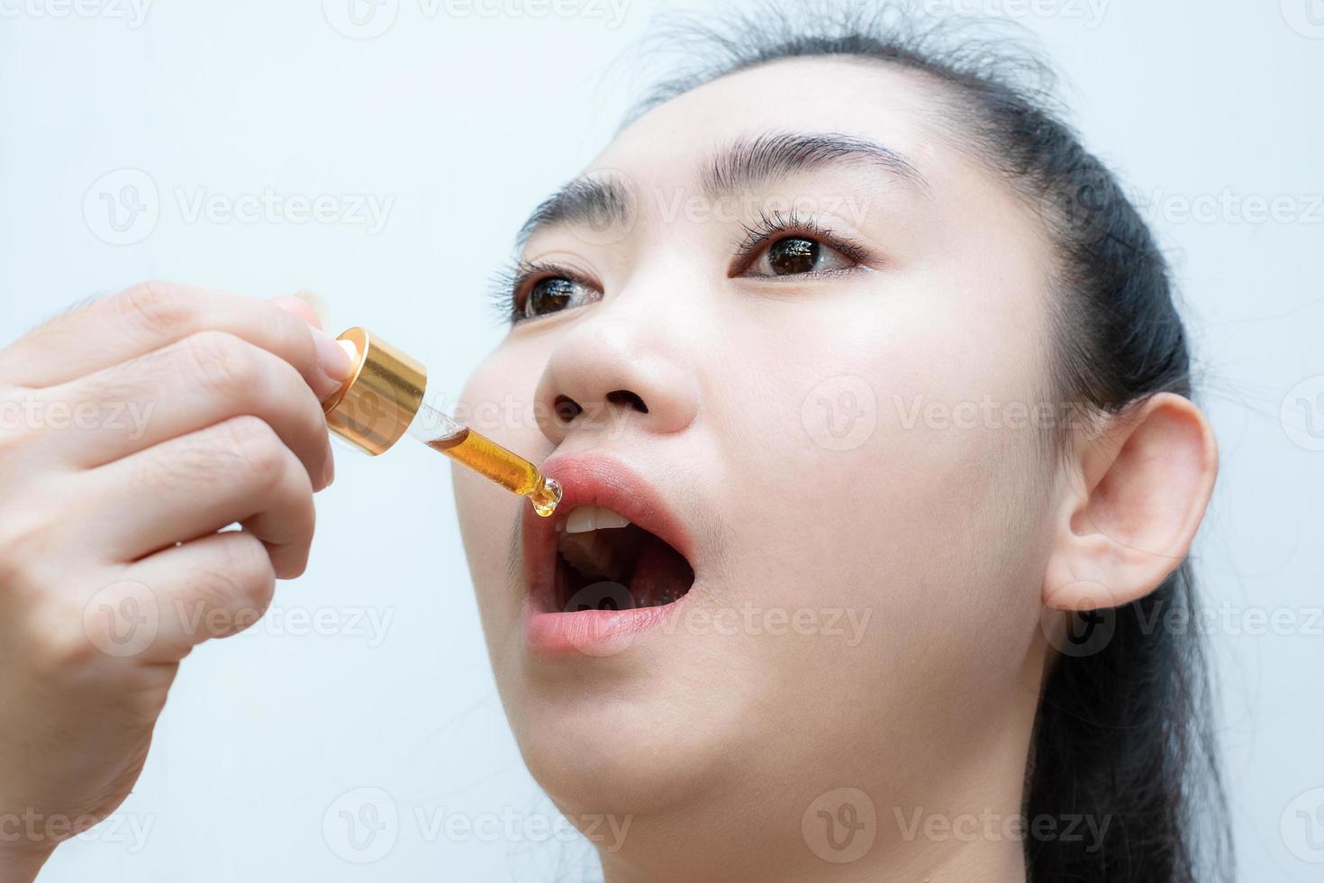 mulher segurando um conta-gotas de óleo de cannabis sublingual em fundo branco foto