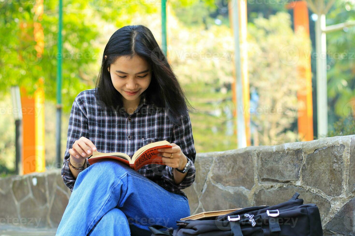 feliz e sucesso fêmea ásia Faculdade aluna desfrutando ler uma livro dentro a parque foto