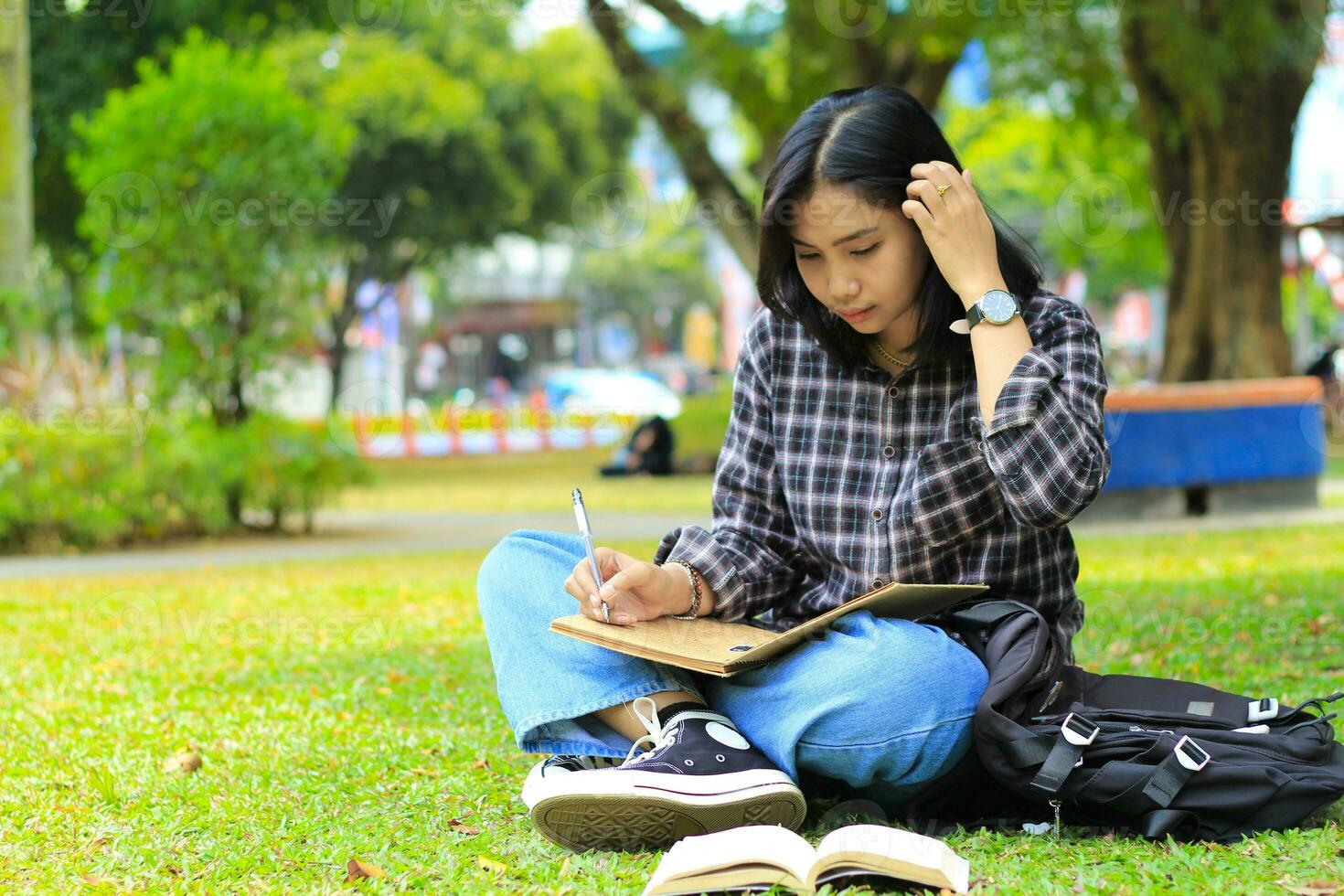 lindo ásia jovem mulher Faculdade aluna focado escrevendo em caderno e lendo livro dentro ao ar livre cidade parque foto