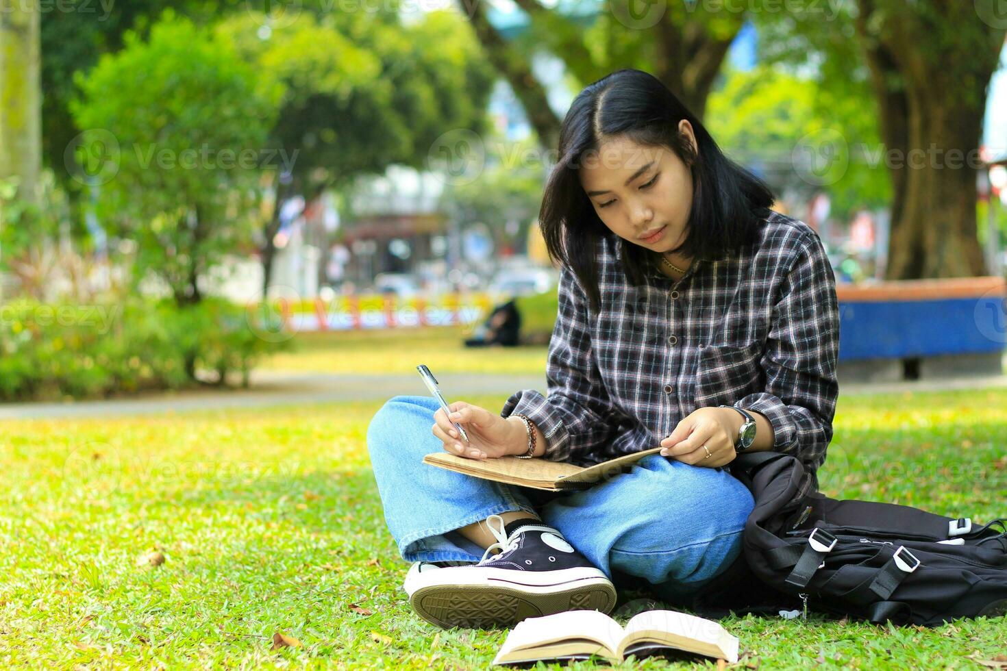 lindo ásia jovem mulher Faculdade aluna focado escrevendo em caderno e lendo livro dentro ao ar livre cidade parque foto